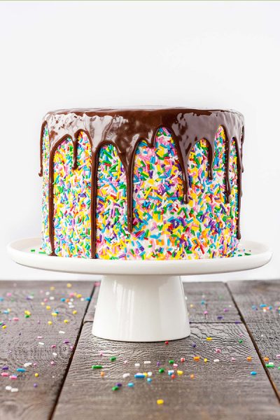 Funfetti Cake - homemade funfetti layer cake filled with sprinkles, topped with fluffy frosting, more sprinkles and a drippy chocolate ganache | by Olivia Bogacki for TheCakeBlog.com