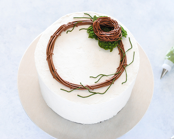 Spring Wreath Cake - how to make a buttercream wreath cake a bird's nest, cherry blossoms, green berries and cookie moss | by Carrie Sellman for TheCakeBlog.com #easter #easterdinnerideas #mothersday #cake